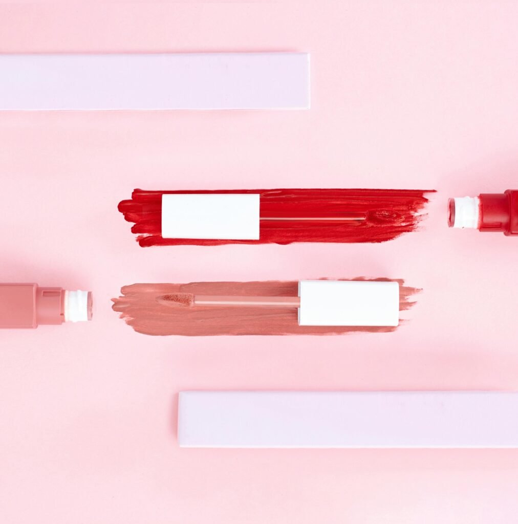 Top view of artistic makeup flatlay showcasing smeared lip gloss on a pink background.